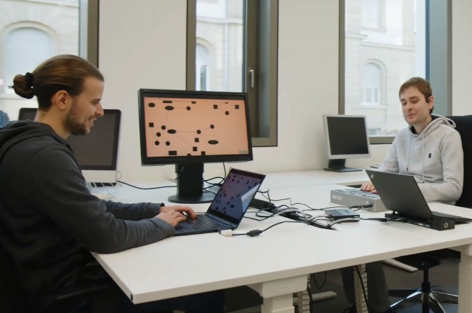 Zwei Personen arbeiten an Laptops in einem hellen Büro mit netzwerkartigen Strukturen auf Bildschirmen.