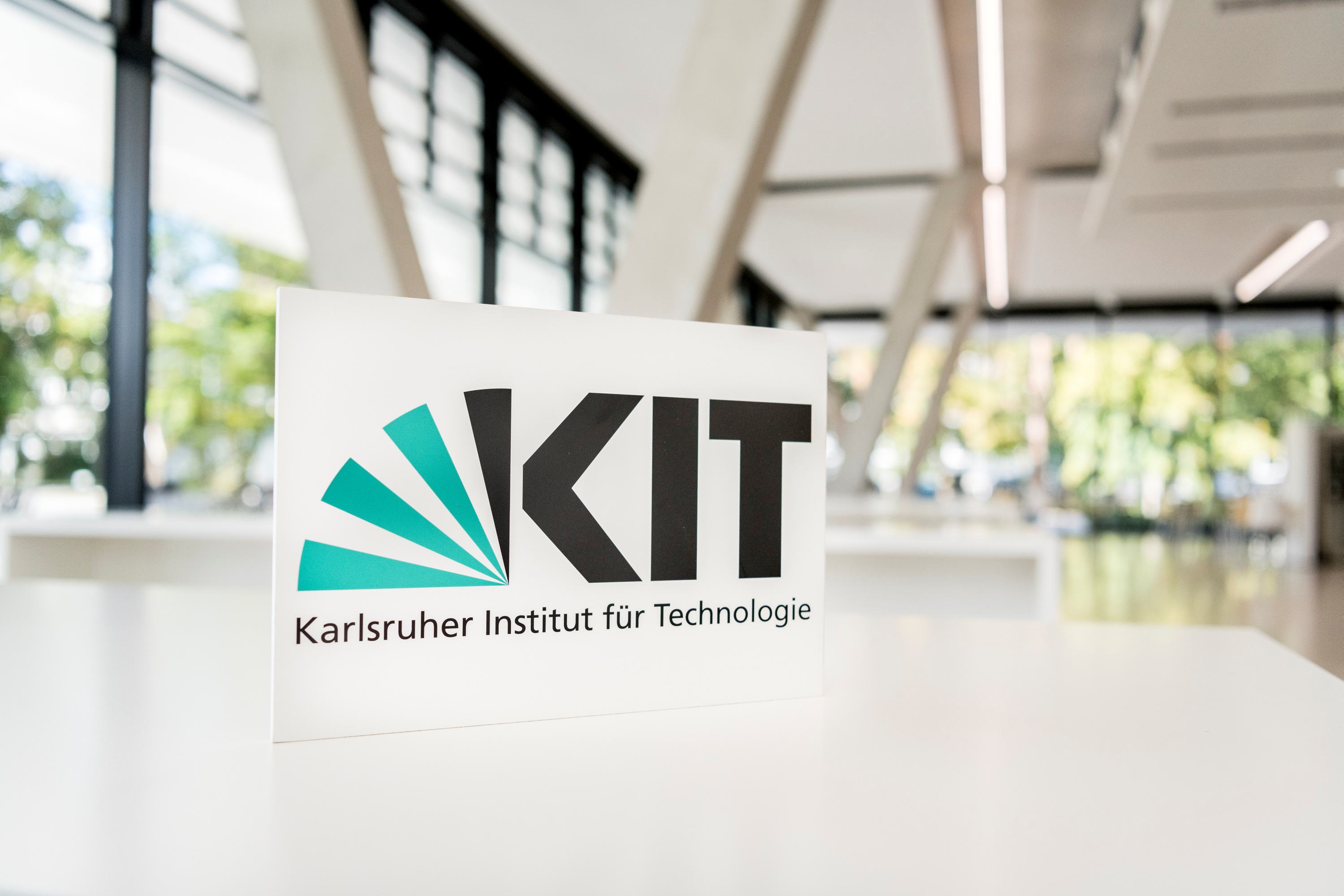 Logo of the Karlsruhe Institute of Technology (KIT) on a white card in a modern building interior.
