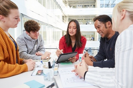 Eine Gruppe junger Erwachsener sitzt um einen Tisch, diskutiert und zeigt auf einem Tablet.