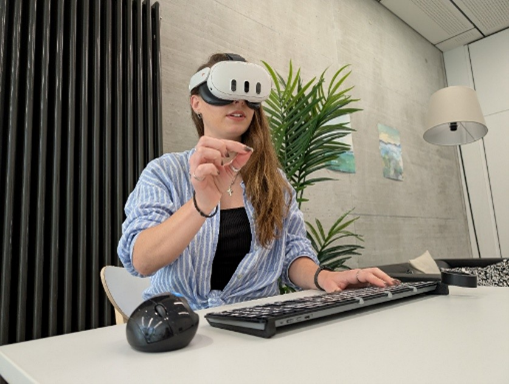 Person mit Virtual-Reality-Headset am Computer, sitzt an Schreibtisch im Büro.